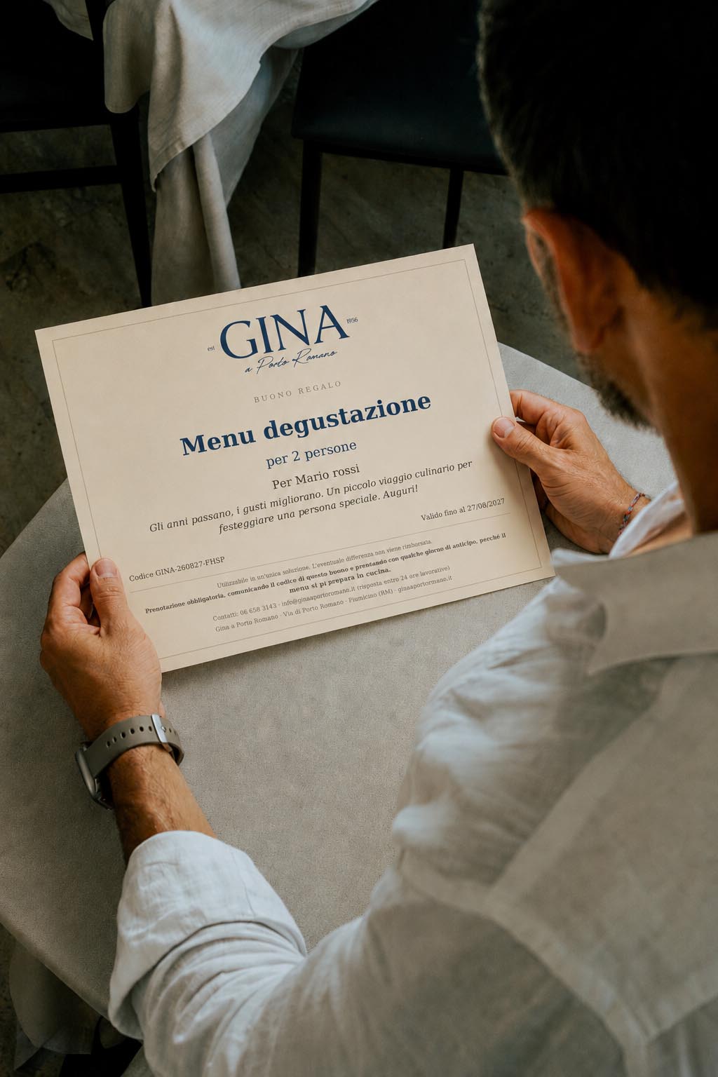 Una persona seduta a tavola tiene tra le mani un buono regalo di Gina a Porto Romano per il menu degustazione per due persone